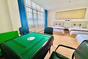 Une chambre d’hôtel équipée d’une table de billard, de deux lits simples, d’une grande fenêtre avec des rideaux bleus et d’une tête de lit ornée d’un motif décoratif.