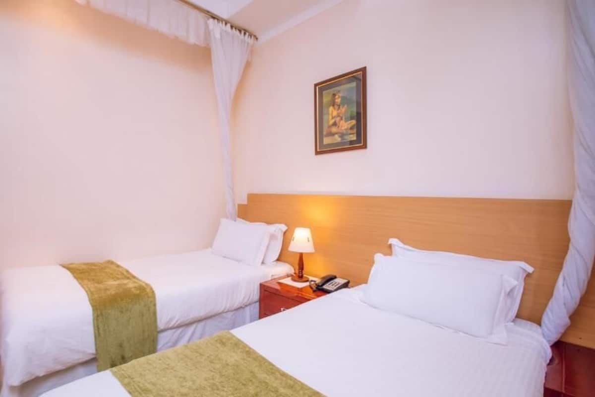 A hotel room with two single beds, a bedside table with a lamp, a phone, and a framed picture on the wall.