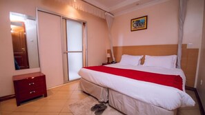 A bedroom with a bed, a nightstand, a dresser, a door, and a painting on the wall. - Longview Residences (Ongata Rongai)