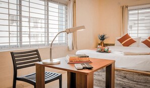 A hotel room with a bed, a bedside table with a lamp, a chair, and a window with blinds. - Ostro Inn (Barasat)