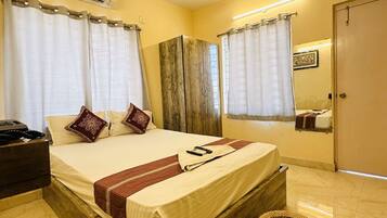 A hotel room with a wooden bed, a bedside table, a small stool, a ceiling fan, and a mirror on the wall.