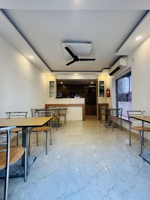 A spacious dining area with marble flooring, multiple tables and chairs, ceiling fans, and an air conditioning unit. - Ostro Inn (Barasat)