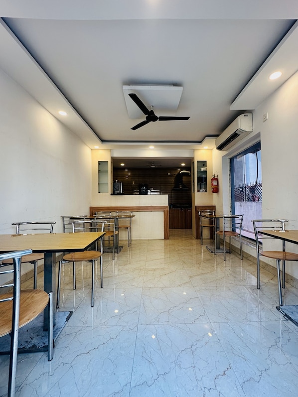 A spacious dining area with marble flooring, multiple tables and chairs, ceiling fans, and an air conditioning unit. - Ostro Inn (Barasat)