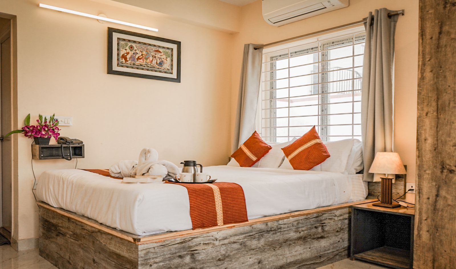 A neatly made bed with a white and orange striped blanket, a bedside table with a lamp, and a window with curtains.