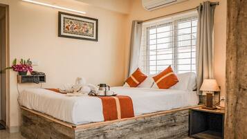 A neatly made bed with a white and orange striped blanket, a bedside table with a lamp, and a window with curtains.
