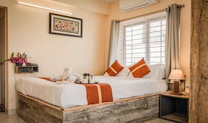 A neatly made bed with a white and orange striped blanket, a bedside table with a lamp, and a window with curtains. - Ostro Inn (Barasat)