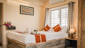A neatly made bed with a white and orange striped blanket, a bedside table with a lamp, and a window with curtains. - Ostro Inn (Barasat)