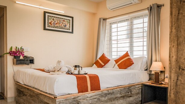 Ein ordentlich gemachtes Bett mit einer weiß-orange gestreiften Decke, ein Nachttisch mit Lampe und ein Fenster mit Vorhängen.