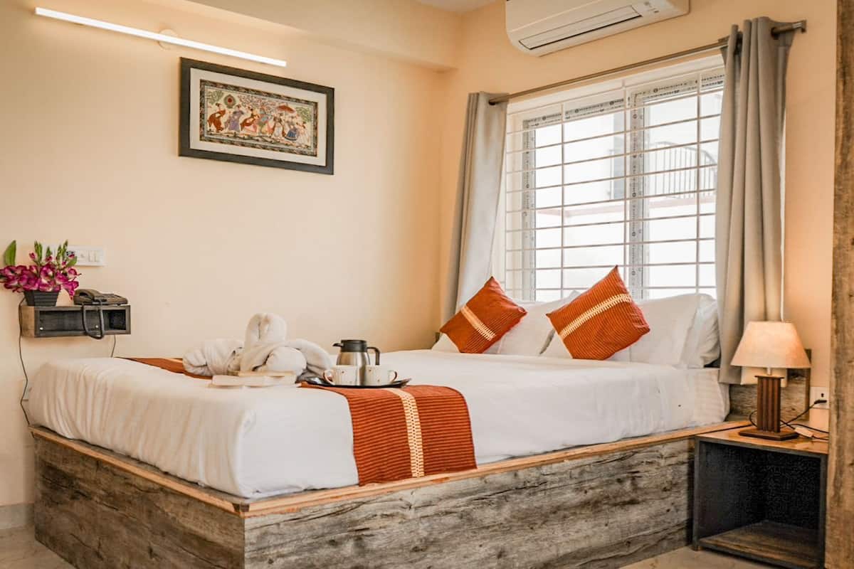 A neatly made bed with a white and orange striped blanket, a bedside table with a lamp, and a window with curtains.