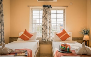 A hotel room with two beds, a window with floral curtains, a lamp, and a tray with snacks. - Ostro Inn (Barasat)