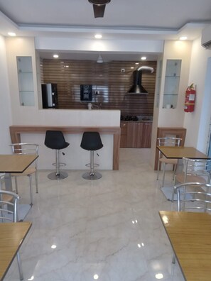 A modern kitchen with a central island, two bar stools, and a fire extinguisher on the wall. - Ostro Inn (Barasat)