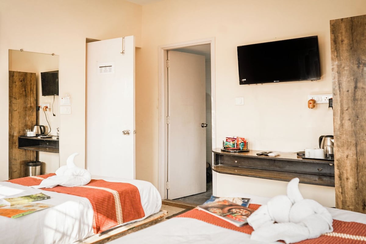 A hotel room with two beds, a TV, a wooden desk, and a door leading to another room.