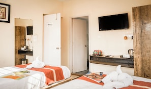 A hotel room with two beds, a TV, a wooden desk, and a door leading to another room. - Ostro Inn (Barasat)
