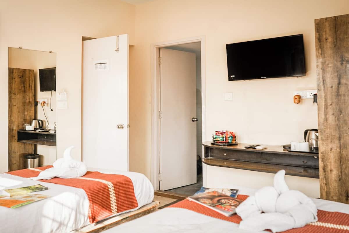 A hotel room with two beds, a TV, a wooden desk, and a door leading to another room.