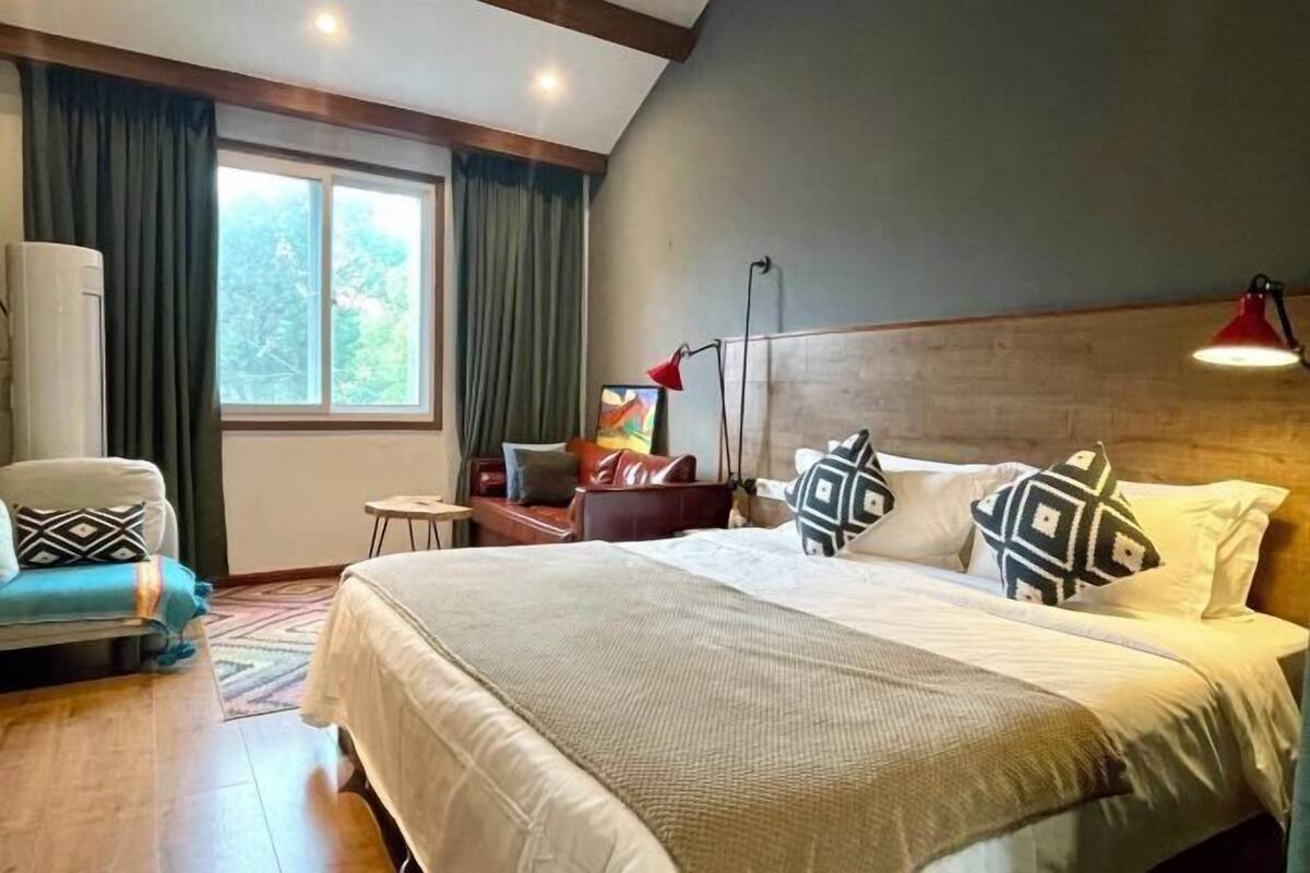 Habitación de hotel con una cama grande, un escritorio, una silla, una ventana con cortinas y una lámpara.