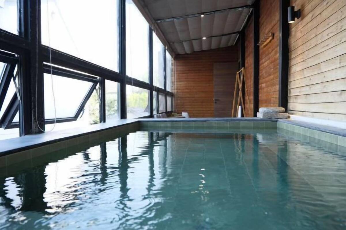 Una piscina interior con paredes de vidrio transparente, paneles de madera en las paredes y una escalera que conduce a una puerta.