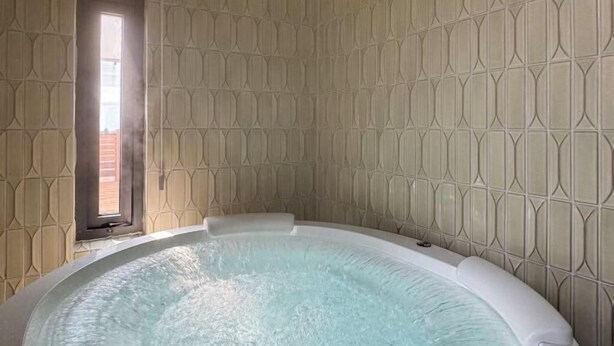 A hot tub in a room with patterned walls and a window.