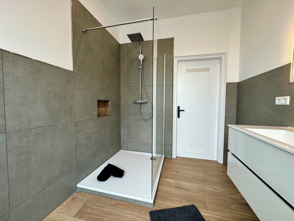 Un baño moderno con cabina de ducha de vidrio, lavamanos blanco y suelo de madera.