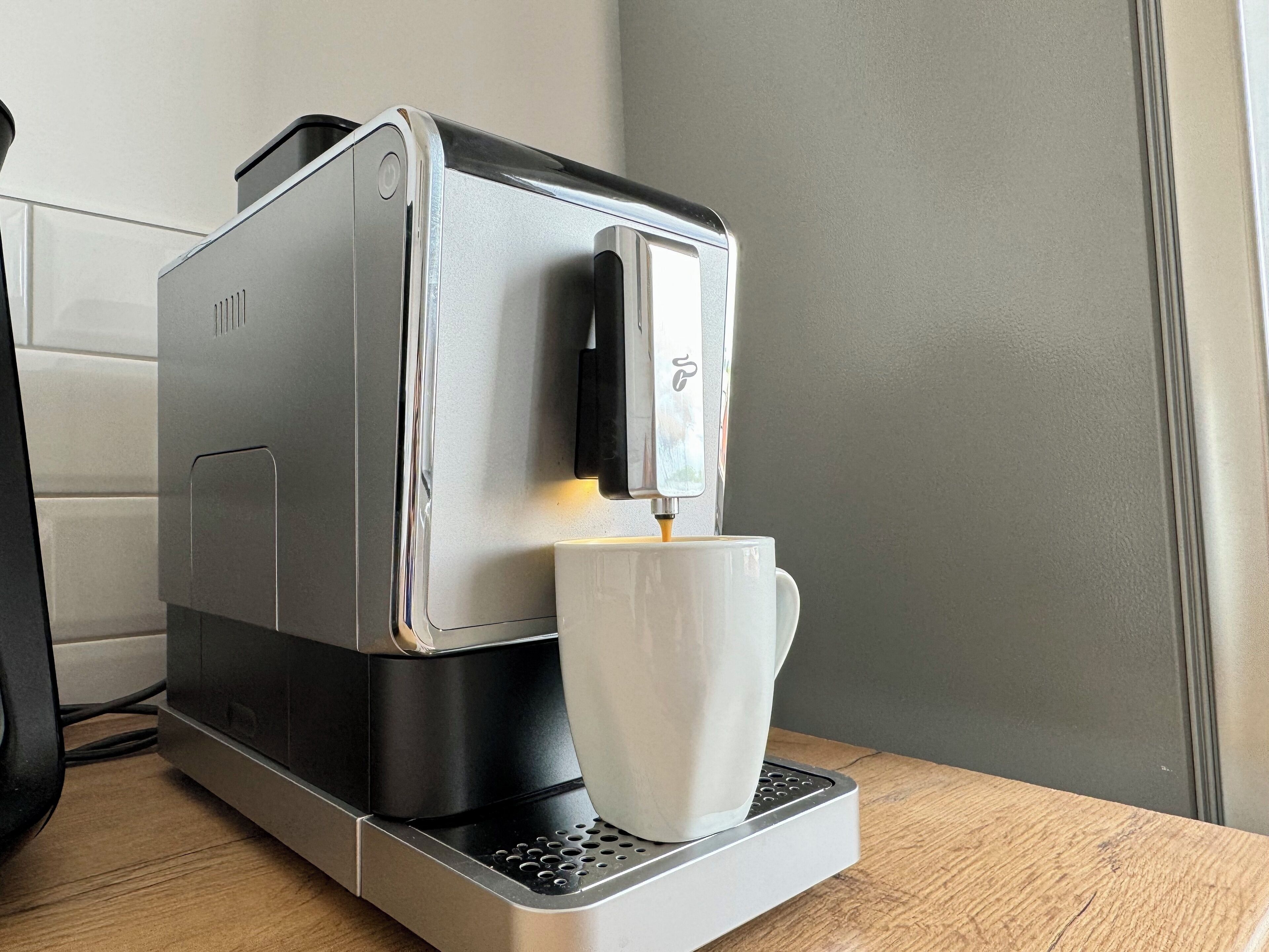 Eine Kaffeemaschine mit einer Tasse darunter auf einer Holztischplatte.