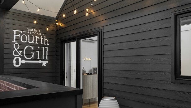 Un intérieur moderne avec un mur en bois foncé, un néon représentant le mot « Cheers », un vase blanc et un banc.