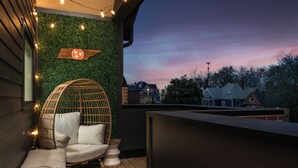 Un balcon avec un fauteuil en osier et des coussins, un mur végétal et une vue sur les maisons au loin.