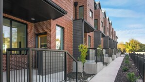 Une rangée de maisons de ville modernes en briques, dotées de grandes fenêtres et bordées d’un étroit trottoir.