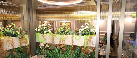 A modern dining area with a long table, cushioned chairs, and hanging plants.