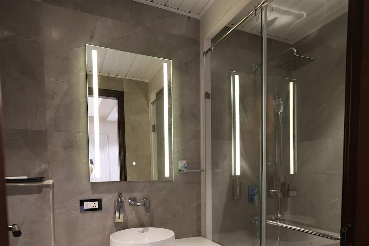 A modern bathroom with a round sink, a large mirror, and a glass-enclosed shower.