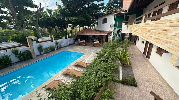 A swimming pool with lounge chairs, surrounded by greenery and a patio area with outdoor furniture. - Pousada Boa Esperança Beach (Ipojuca)