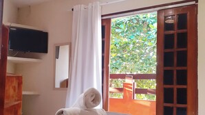 A hotel room with a bed, a TV mounted on the wall, a window with curtains, and a view of greenery outside. - Pousada Boa Esperança Beach (Ipojuca)
