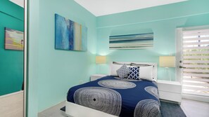 A bedroom with a bed, two bedside lamps, a painting on the wall, and a window with blinds.