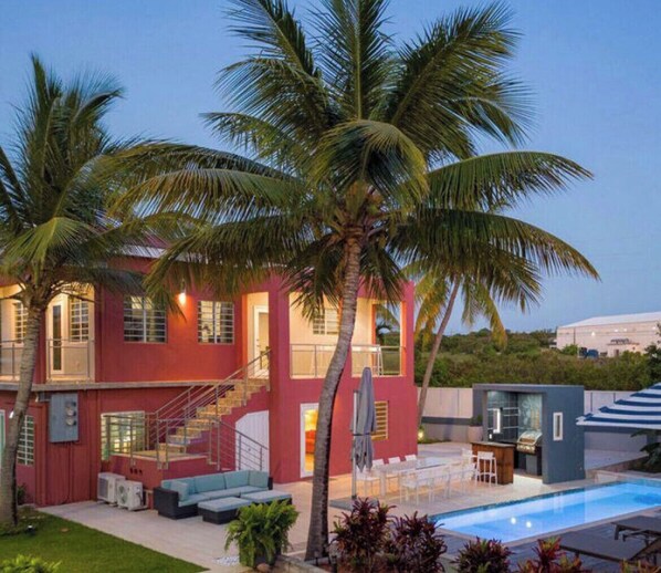 Uma casa de dois andares com fachada vermelha, piscina e palmeiras.