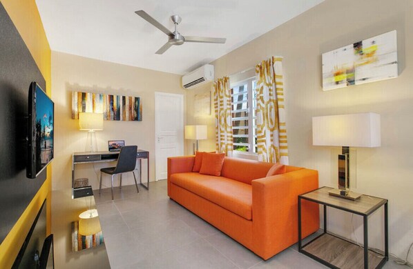 A modern hotel room with a sofa, desk, chair, and a television.