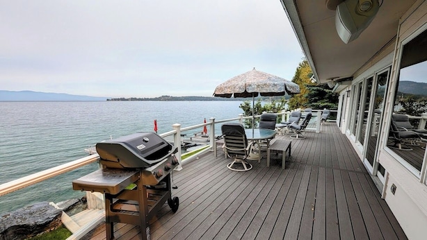 Um terraço com churrasqueira, móveis de exterior e vista para a água.