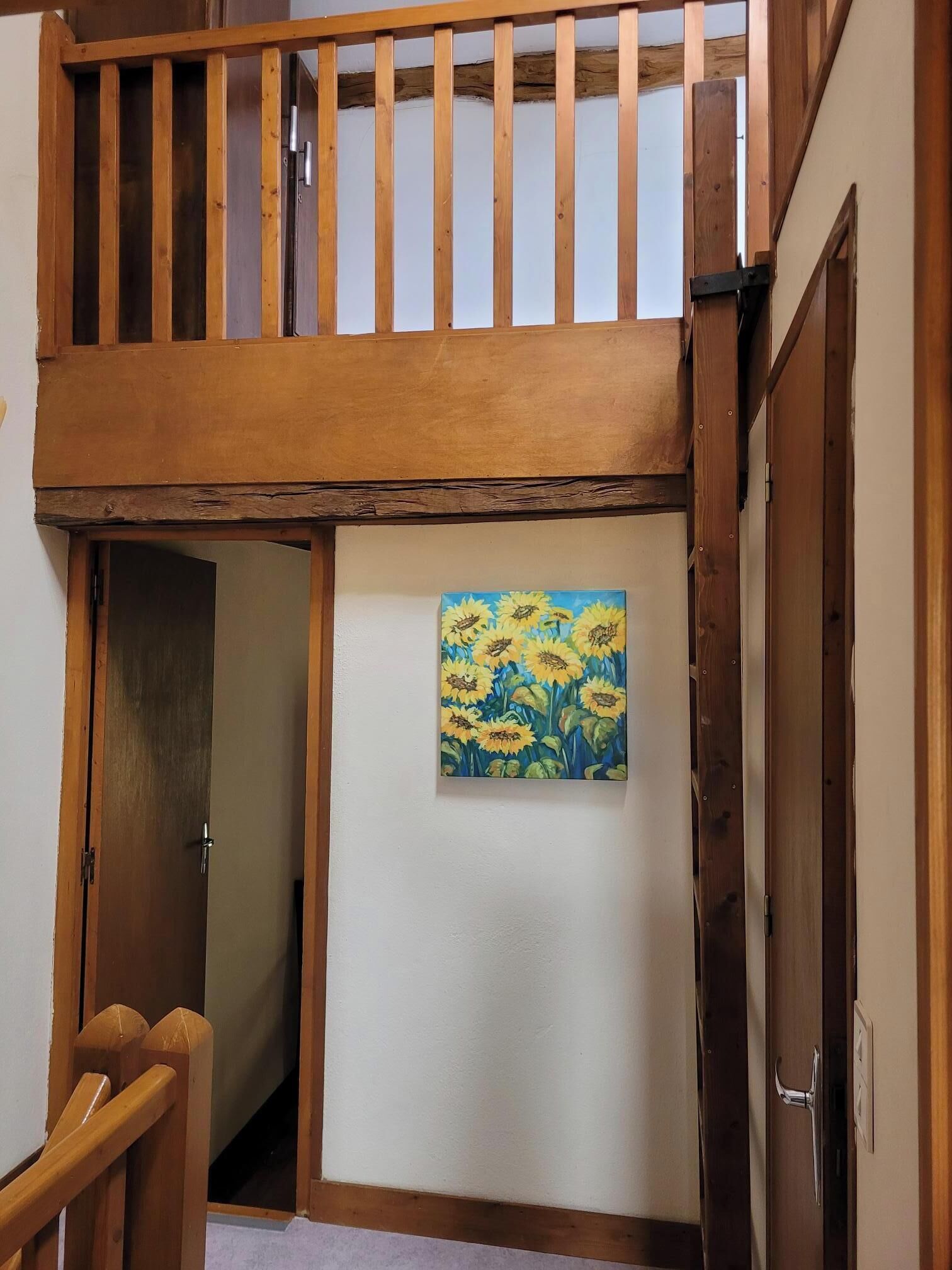 A wooden staircase with a glass door leading to a room with a painting of sunflowers.
