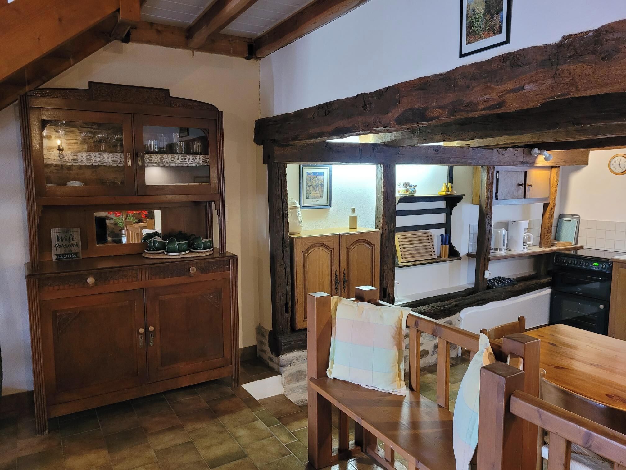 A rustic kitchen with wooden cabinets, a dining table, and a view into the adjacent dining area.