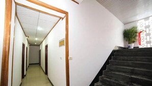 A hallway with a wooden door frame, a staircase with a black handrail, and a potted plant on the right. - Fenghua Hotel (Yichang)
