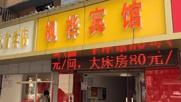A hotel with a bright yellow sign and red neon lights advertising room rates. - Fenghua Hotel (Yichang)