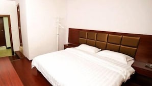 A hotel room with a large bed, a wooden headboard, a nightstand, and a wooden desk. - Fenghua Hotel (Yichang)