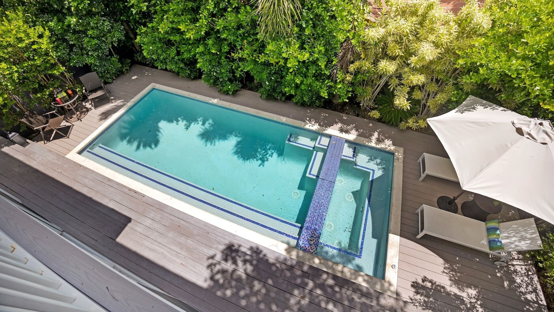 Une piscine rectangulaire dont les bords sont recouverts de carreaux, entourée d’une terrasse en bois.