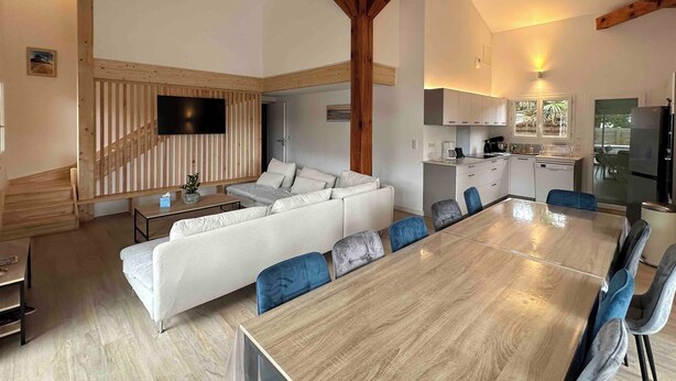 Amplia sala de estar con techo de madera, un sofá blanco, una mesa de comedor con sillas y una zona de cocina con armarios y un refrigerador.