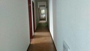 Ein schmaler, mit Teppich belegter Korridor mit weißen Wänden und roten Türen, der zu einem Zimmer mit Fenster führt.