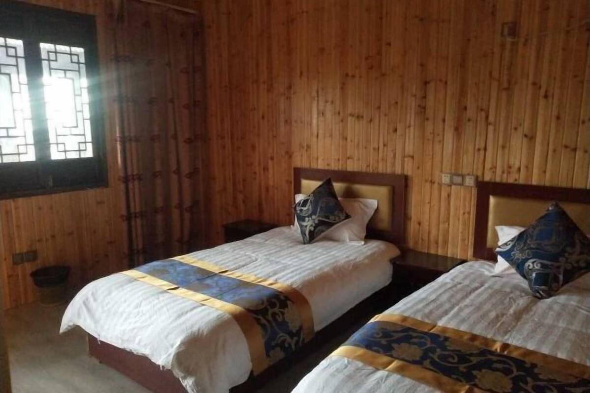 Une chambre avec deux lits, des murs en bois et une fenêtre ornée d’un motif géométrique.