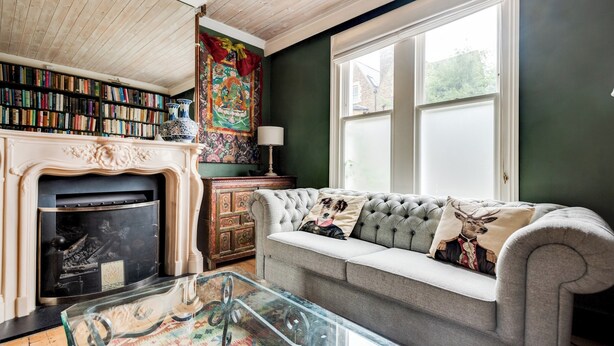 Una sala de estar acogedora con chimenea, un sofá con cojines decorativos, una estantería y un ventanal grande.