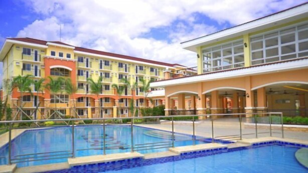 A hotel with a swimming pool, multiple balconies, and a large building with a red roof. - Lian's Haven at Arezzo Place Davao (Davao City)