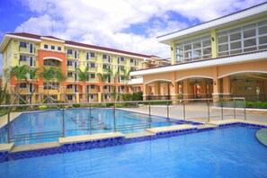 A hotel with a swimming pool, multiple balconies, and a large building with a red roof. - Lian's Haven at Arezzo Place Davao (Davao City)