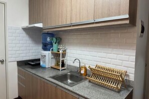 A kitchen with a granite countertop, stainless steel sink, wooden cabinets, and a built-in shelf with kitchen items. - Lian's Haven at Arezzo Place Davao (Davao City)