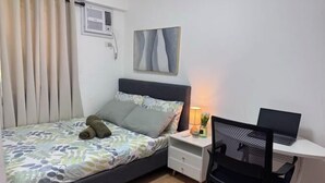 A bedroom with a bed, a desk with a laptop, a chair, a bedside table, and a wall-mounted air conditioner. - Lian's Haven at Arezzo Place Davao (Davao City)