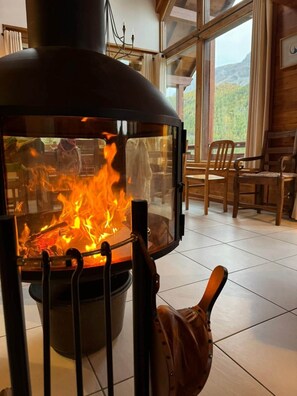 Un poêle à bois avec un feu, une vue sur l’extérieur et un coin repas avec des chaises et une table.