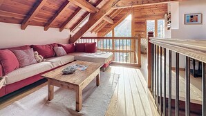A cozy loft bedroom with a wooden ceiling, a red sofa, a wooden coffee table, and a view of the outdoors. - Chalet face aux étoiles (Molines-en-Queyras)